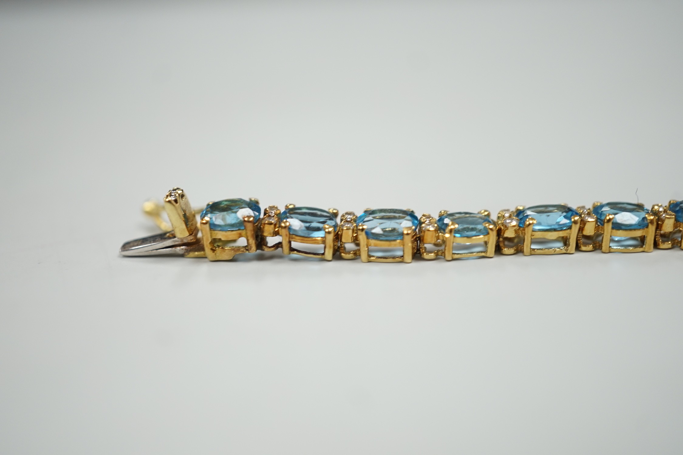 A modern 750 yellow metal and blue topaz set line bracelet, with diamond chip spacers, 17.75cm